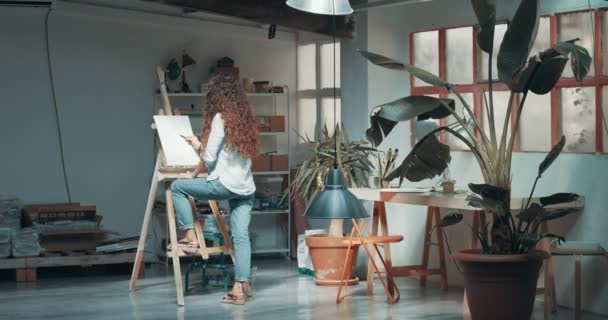 Cute red-haired girl paints in her studio — Stock Video