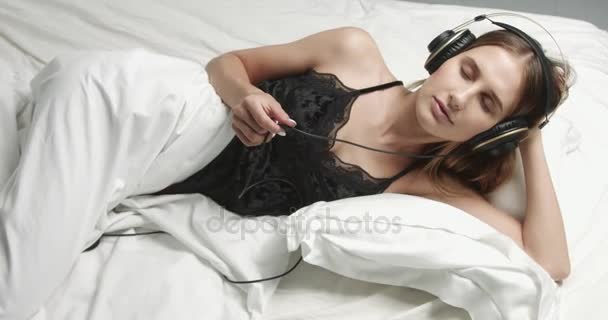 Чувственная женщина в постели с большими наушниками — стоковое видео