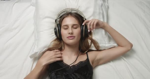 Αισθησιακή γυναίκα στο κρεβάτι με μεγάλα ακουστικά — Αρχείο Βίντεο