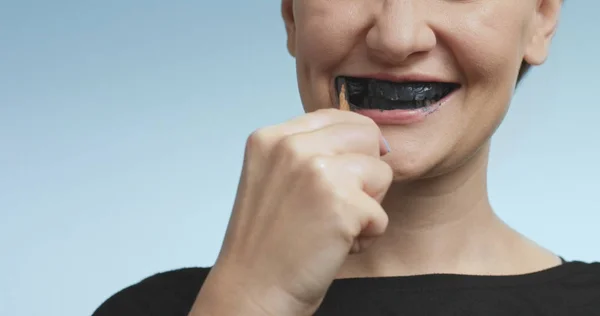 Pretty young woman brushing her teeth with black toothpaste — Stock Photo, Image