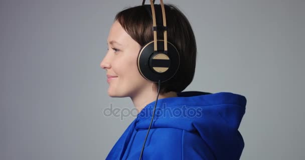 Schöne Frau in blauem Kapuzenpulli setzt Kopfhörer auf — Stockvideo