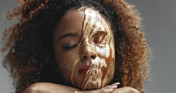 Black model with curly hair and a liquid facial makeup base pouring on her face — Stock Video