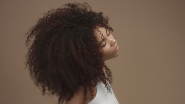 Женщина смешанной расы трясет волосами и трогает их, смотрит в камеру — стоковое видео