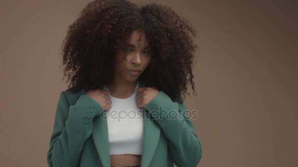 Черная женщина смешанной расы в зеленом пальто на бежевом фоне с огромными вьющимися африканскими волосами — стоковое видео
