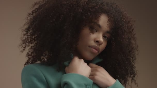 Gemengd ras zwarte vrouw in groene jas in beige achtergrond met enorme krullend afro haar — Stockvideo