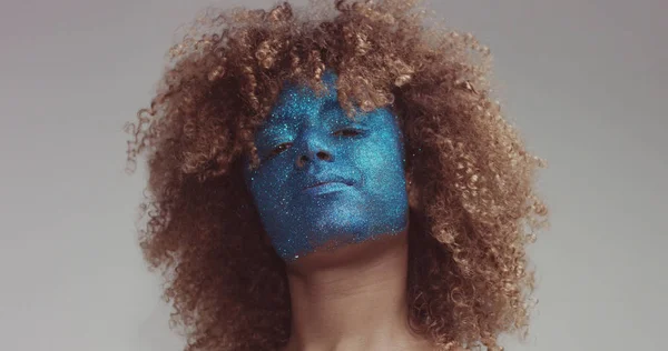 black woman with blond hair and blue glitter face makeup