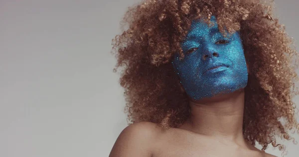 black woman with blond hair and blue glitter face makeup