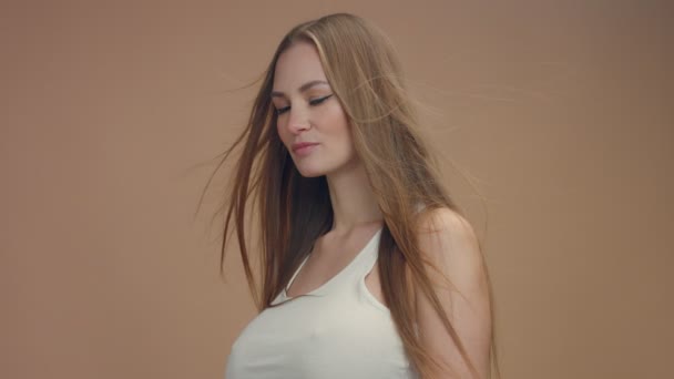 Modelo de mujer de belleza en estudio sobre fondo beige con viento en el pelo soplando — Vídeo de stock