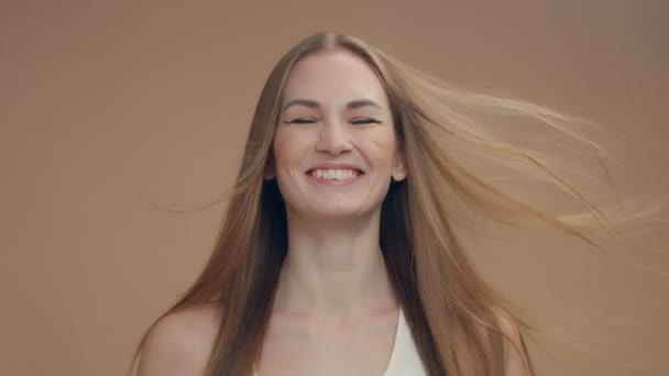 Красива жінка модель в студії на бежевому фоні з вітром у волоссі збиває його — стокове відео