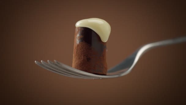 Una caramella al cioccolato sulla forchetta ricoperta di crema bianca, cadendo lentamente — Video Stock