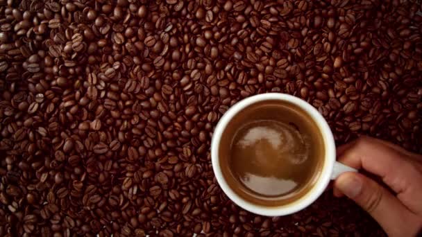 Vue de dessus de la main avec tasse de café noir le mettre sur fond de grains de café — Video