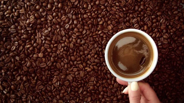 Bovenaanzicht van de hand met kopje zwarte koffie zet het op koffie bonen achtergrond — Stockfoto