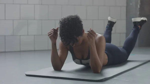 Jonge pasvorm en Toon omhoog vrouw liggend ontspannen heeft een rust tijdens haar fitnesstraining met plank elementen voor Spierversterkend abs in zonnige loft — Stockfoto