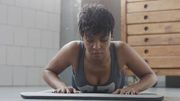 Jeune ajustement et tonifier femme faisant entraînement de remise en forme avec des éléments de planche pour abdos tendus dans loft ensoleillé — Photo