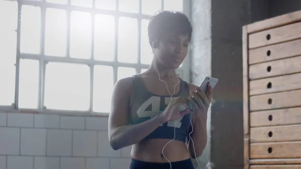 Ung passar och tona upp kvinna gör fitness workoutand att välja en låt i smartphone — Stockfoto