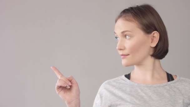 Жінка портрет на сірий показ пальцем У бік і дивлячись на цьому напрямку — стокове відео