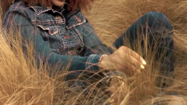 Mujer de raza mixta negra con pelo rizado afro grande en el campo de césped con hierba de heno de otoño seca alta y luz del atardecer — Vídeos de Stock