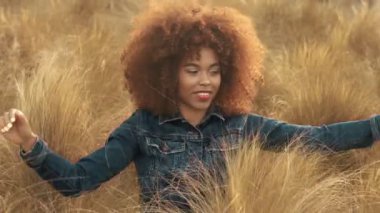 çim alan yüksek kuru sonbahar saman çim ve günbatımı ışığı ile büyük afro kıvırcık saçlı siyah karışık ırk kadın