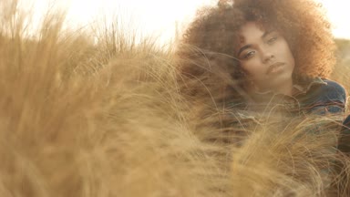 çim alan yüksek kuru sonbahar saman çim ve günbatımı ışığı ile büyük afro kıvırcık saçlı siyah karışık ırk kadın