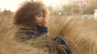 çim alan yüksek kuru sonbahar saman çim ve günbatımı ışığı ile büyük afro kıvırcık saçlı siyah karışık ırk kadın