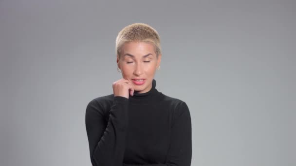 Блондинка з короткою стрижкою в студійних позах для камери на сірій ідеальній шкірі — стокове відео