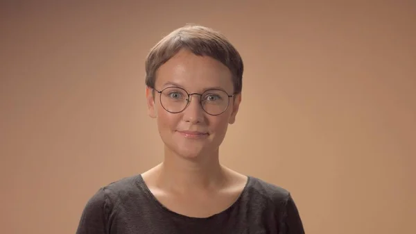 Белая женщина с короткой стрижкой носит очки в студии на бежевом фоне — стоковое фото