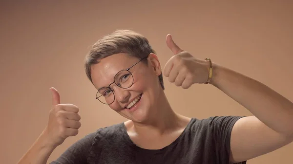 Kaukasische Frau mit Kurzhaarschnitt trägt im Studio eine Brille auf beigem Hintergrund — Stockfoto