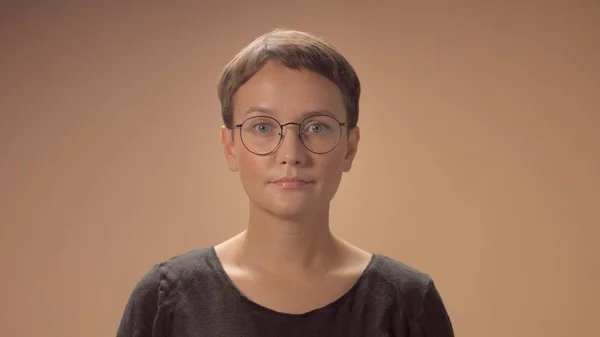 Kaukasische Frau mit Kurzhaarschnitt trägt im Studio eine Brille auf beigem Hintergrund — Stockfoto