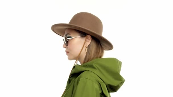 Женщина осенью смотрит в студию в зеленой парке и шляпе поворачивается и позирует перед камерой — стоковое видео