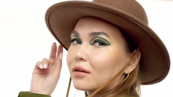 Frau im Herbstlook im Atelier in grünem Parka und Hut dreht sich um und posiert vor der Kamera — Stockvideo