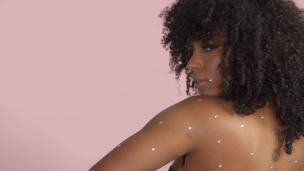 Smíšené závod černá žena s kudrnaté vlasy pokryté křišťálovým make-upem na růžovém pozadí ve studiu — Stock video