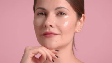 30 'lu yaşlardaki esmer kadın pembe arka planda stüdyo için ideal cilde sahip dekolte bir bluz giyiyor.