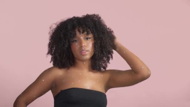 Mixed race black woman with curly hair covered by crystal makeup on pink background in studio — Stock Video