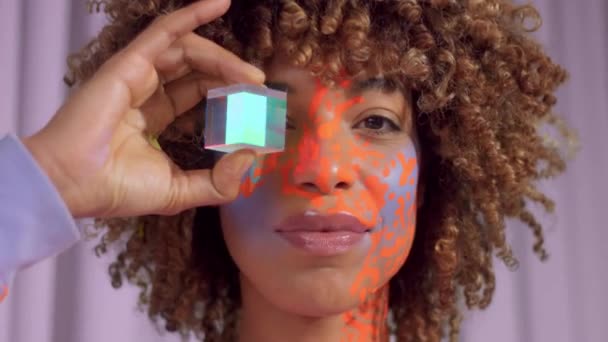 Gemengde race vrouw met krullend haar en heldere neon make-up patroon op het gezicht hetzelfde als op haar sweater — Stockvideo