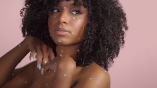 Μικτή φυλή μαύρη γυναίκα με σγουρά μαλλιά καλύπτονται από κρύσταλλο μακιγιάζ σε ροζ φόντο στο στούντιο — Αρχείο Βίντεο