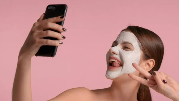 30s brunette woman with a facial clay mask on making selfie with a smartphone — Stock Photo, Image