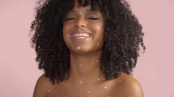 Μικτή φυλή μαύρη γυναίκα με σγουρά μαλλιά καλύπτονται από κρύσταλλο μακιγιάζ σε ροζ φόντο στο στούντιο — Φωτογραφία Αρχείου