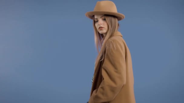Blond model rollend op diepblauwe achtergrond in grote jas — Stockvideo