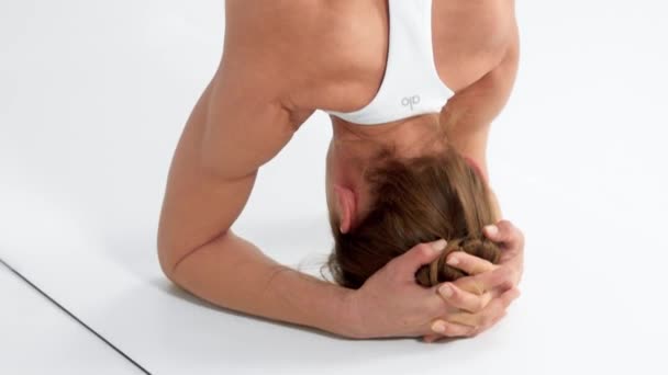 Mujer mayor en el espacio blanco practica yoga hace un soporte de cabeza — Vídeos de Stock