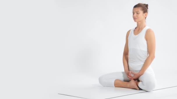 Mujer mayor en el espacio blanco practica yoga se sienta en posición de loto — Vídeo de stock