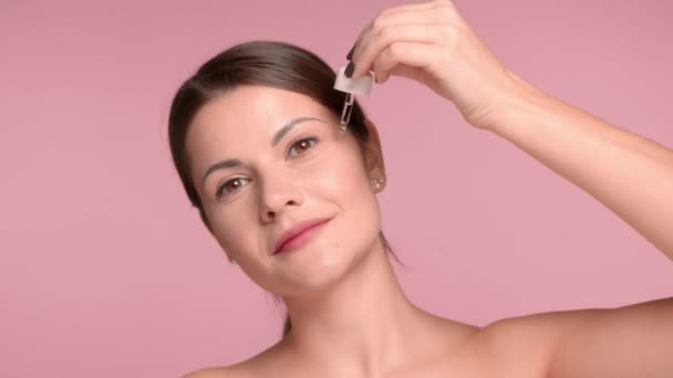 30s brunette woman closeup with an oil dropper put some oil on her cheek wear a decollete top — Αρχείο Βίντεο