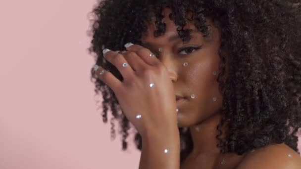 Mujer negra de raza mixta con pelo rizado cubierto de maquillaje de cristal sobre fondo rosa en el estudio — Vídeo de stock