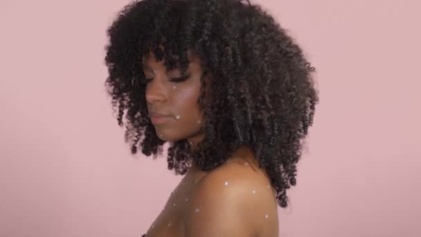 Razza mista donna nera con i capelli ricci coperti da trucco di cristallo su sfondo rosa in studio — Video Stock
