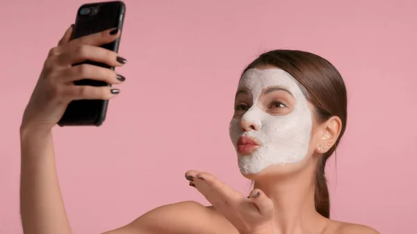 30s brunette vrouw met een gezicht klei masker op het maken van selfie met een smartphone — Stockfoto