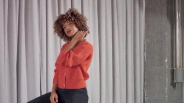 Mixed race woman on grey curtains background sits on chair and dancing