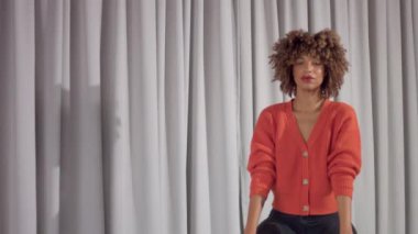 Mixed race woman on grey curtains background sitson chair and poses to camera