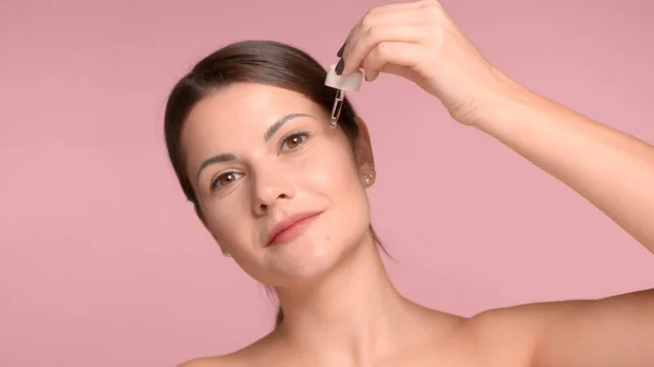 30s bruna donna guardando da parte mettere alcuni cosmetici con un contagocce alla sua zona guancia — Foto Stock