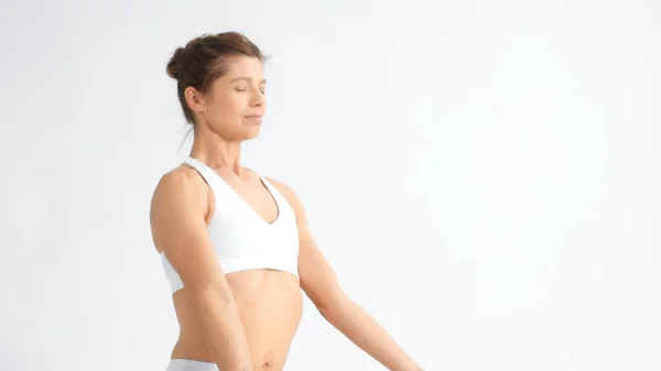 Senior woman in white space practice yoga sits in lotus pose with eyes closed — ストック写真