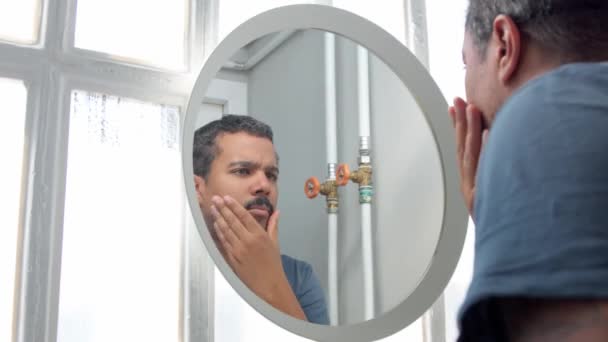 Homem atrás do espelho durante sua rotina de cuidados faciais matinais observando a si mesmo — Vídeo de Stock