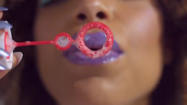Смешанная женщина расы с фиолетовым блестящим блеском помады на ударах пузыря воздуходувка к камере — стоковое видео